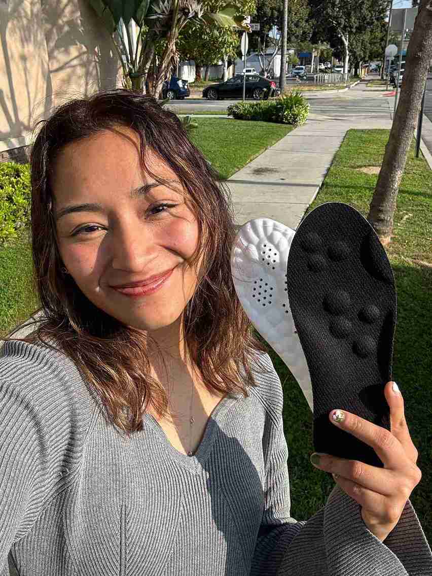 Woman holding two shoe inserts outdoors on a sunny day